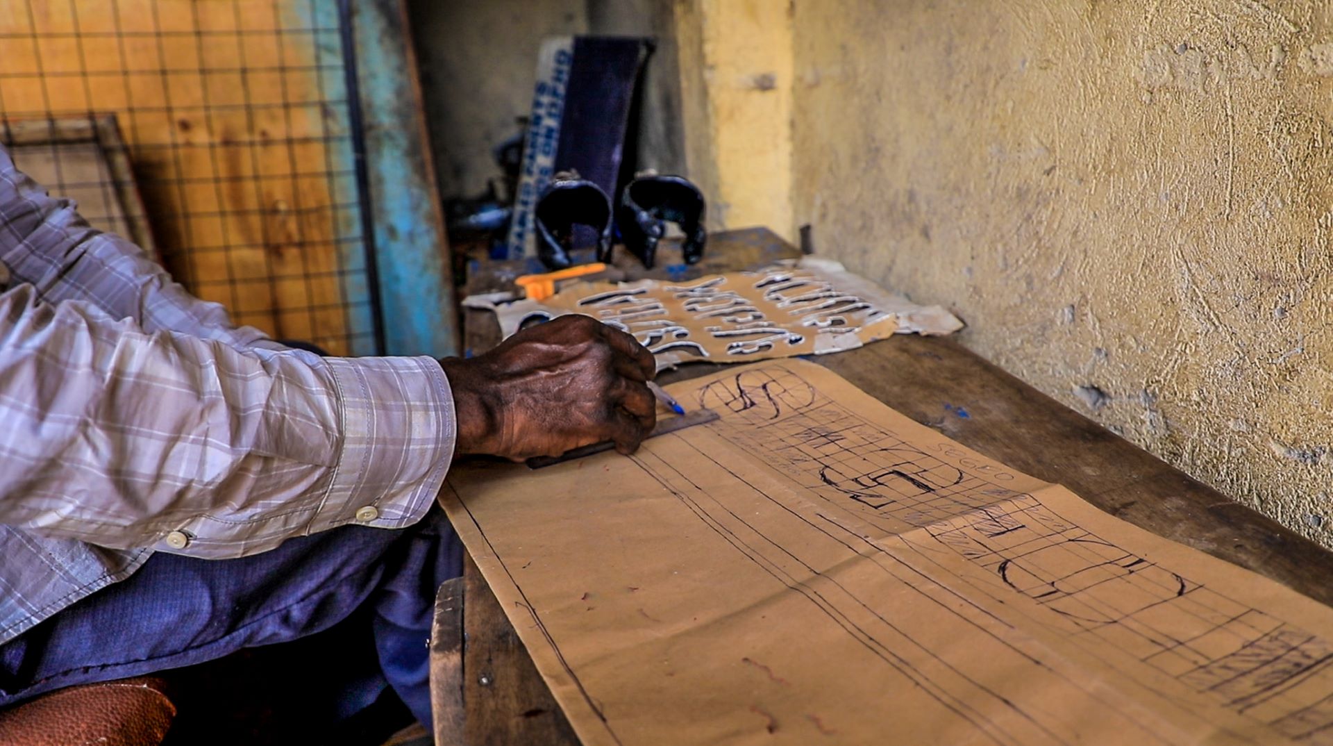 Lawrence Renco Kasirye crafts out letter as he prepares to make signages. Lawrence is grateful to the Kulea Watoto Project for supporting him with financial literacy trainings and a cash grant that enabled him to re-establish his business and support his family  