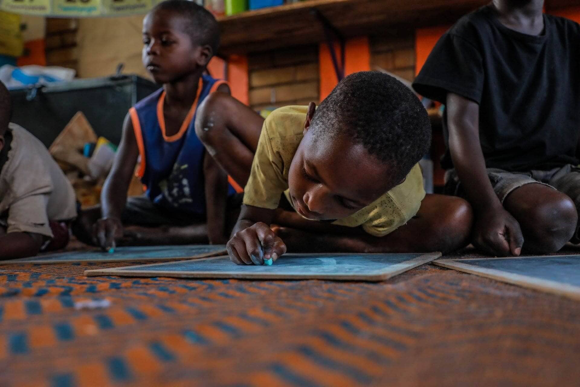 Cynthia Ngonga in class, excited to learn to draw, color, and write - things she can't do at home. She’s made many friends, enjoys playtime, and no longer worries, knowing she'll get porridge at school.