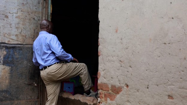 Kiberu Hassan, Chairperson - CMC at Kiti Nursery School, jumps over the raised flood barrier at the class entrance designed to control surface runoff and protect the premises from floodwaters